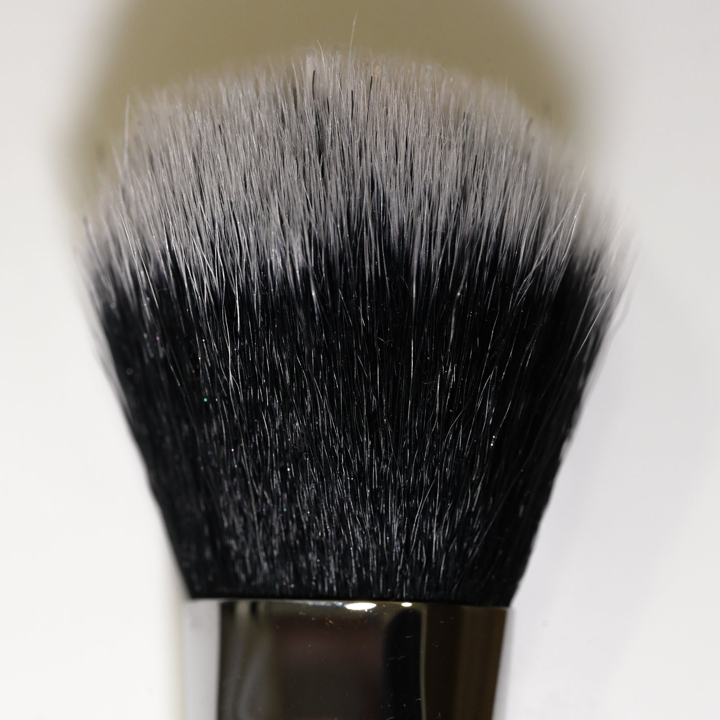 Close-up of a round makeup brush with black and white synthetic bristles and a silver metal ferrule.