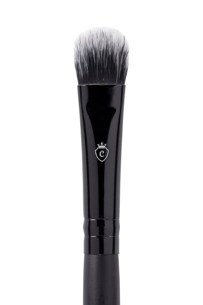 Black makeup brush with a flat, rounded head, white-tipped bristles, and a silver crest logo on the handle.